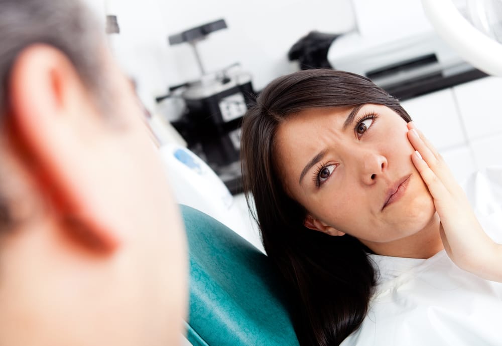 A woman in a dental chair holding her cheek, indicating discomfort, speaking with a dentist - Dentist Columbus Ohio​​ 